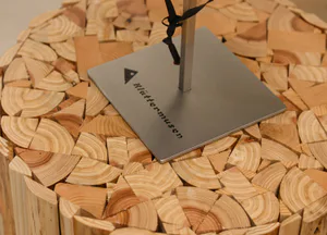 Close-up view of a handmade side table made from natural pine wood slices with a square brushed steel base branded Klattermusen.