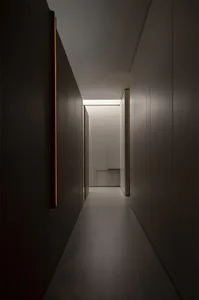 Long, narrow minimalist hallway featuring dark wood paneling, seamless light-colored cabinetry, and dramatic linear ceiling lighting creating strong contrast and depth.