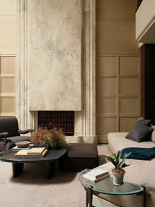 Luxurious living room featuring a towering marble fireplace, dark sculptural coffee table, neutral sofa with deep teal accents, and layered neutral textures.