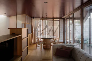 現代簡約餐廳，設有圓形玻璃桌面餐桌、淺木色椅子、嵌入式木質櫃體、米色肌理沙發搭配酒紅抱枕，以及通往戶外露台的大型滑門。