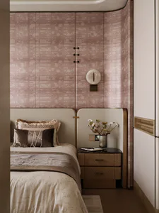 Modern luxury bedroom interior with pinkish-taupe patterned wallpaper, curved architectural wall, upholstered headboard, walnut nightstand, and decorative wall sconce.