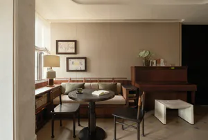Serene living room featuring a dark walnut upright piano, built-in striped banquette with green cushions, round dark table, and wooden chairs in soft natural light.