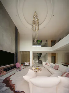 Modern luxury living room with double-height ceiling, large white sectional sofa, pink accent chair, gold statement chandelier, and marble floor with custom rug.