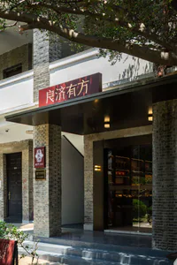 傳統中式老字號茶莊白天外觀，灰磚柱、白牆、深色金字招牌「良濟有方」，搭配現代玻璃展示櫥窗。