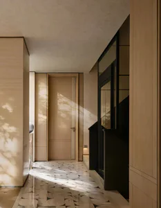 Modern minimalist hallway featuring light oak wood paneling, black-framed glass doors, and a geometric patterned marble floor bathed in natural sunlight with tree shadows.