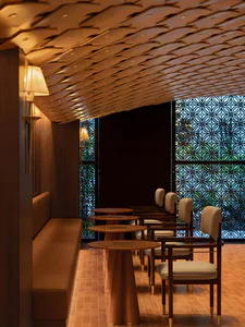 Interior view of a sophisticated Japanese-style restaurant featuring a long upholstered banquette, round wooden pedestal tables, and matching armchairs with cream upholstery, all beneath an elaborate sculptural wooden ceiling with integrated lighting and decorative lattice window screens in the background.