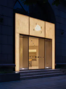 夜間現代極簡店面，外牆使用大面積背光洞石板材，大面積玻璃入口，品牌名稱 Yeye 清晰呈現於立面與階梯上。