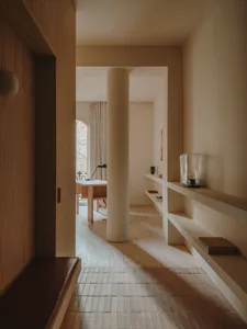 Minimalist modern entryway featuring light oak wood paneling, a built-in leather bench, a structural column, and white floating shelves with decorative objects.