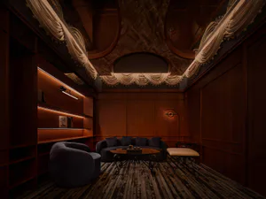 Luxurious home theater room featuring dark walnut wood paneling, built-in LED-lit shelving, a curved dark blue velvet sofa, a round coffee table with ornate metal base, and an elaborately draped fabric ceiling treatment.