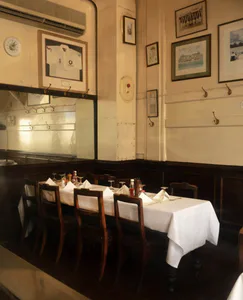 Interior view of a traditional British-style restaurant dining room featuring a long white-clothed table, dark wood chairs, and walls decorated with framed cricket memorabilia including signed jerseys.