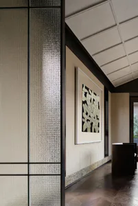 Modern interior hallway with textured glass partition on the left, large framed abstract black and white artwork on the wall, dark wood flooring, and a cylindrical dark console table under a coffered ceiling.