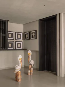 Modern minimalist entryway featuring two large vintage wooden pelican sculptures, framed tribal masks on the wall, and a dark textured front door.