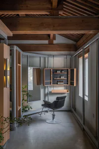 Modern industrial loft hair salon interior with exposed wooden ceiling beams, polished concrete floor, black Eames-style barber chair, and wooden wall cabinet.