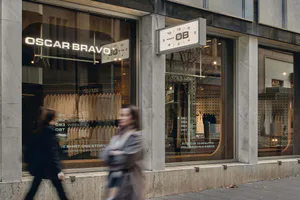 Oscar Bravo 現代極簡零售店面，白色大理石柱、大面積玻璃窗、霓虹招牌，以及走過的模糊行人。