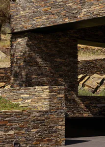 Close-up view of a rustic natural stone pillar and horizontal overhang with textured masonry walls under bright sunlight.