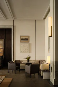 Modern luxury living room with beige sectional sofa, dark leather armchairs, marble side tables, contemporary wall art, and warm wall sconce lighting.