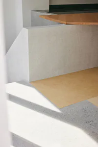 Close-up view of a modern split-level staircase featuring raw concrete structure and light oak wooden flooring with strong natural shadows.