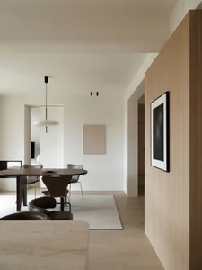 Modern minimalist dining room featuring a dark oak oval table, brown leather chairs, a large white pendant lamp, light oak wall paneling, and a neutral area rug.