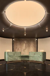 Luxurious hotel or office lobby featuring a curved green marble reception desk, metallic tree mural wall, dark patterned floor with gold inlays, and a dramatic dark ceiling with a large illuminated oval opening and crystal spotlights.