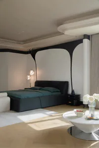 Modern minimalist bedroom featuring a dark teal velvet platform bed, curved black accent wall, two spherical pendant lights, white round coffee table, and light wood flooring.