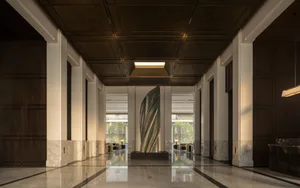 Symmetrical view of a modern luxury hotel lobby with polished marble floors, dark wood paneling, coffered ceiling with skylight, and a tall twisted bronze sculpture in the center.