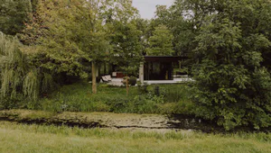 Modern glass house with concrete elements situated beside a lily pad covered pond in a dense forest setting