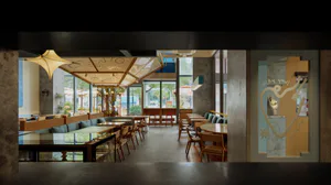 Modern cafe interior viewed from the entrance, showing wooden tables and chairs, teal booth seating, large glass windows, concrete pillars, and a decorative heart-shaped door with the text 'lucky you' on the right side.