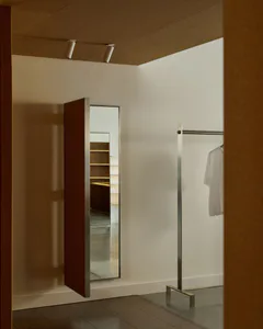 Modern minimalist entryway featuring a large red pivot door with stainless steel frame, concrete terrazzo floor, white walls, and a stainless steel clothing rack with a white t-shirt.