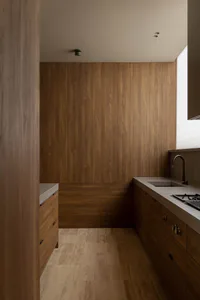 Modern minimalist kitchen interior with warm wood walls, concrete countertops, wooden cabinetry, and a black faucet next to a window with blinds.