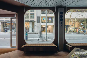 Modern retail interior featuring large arched windows, dark walnut wood paneling, built-in tufted brown benches, and a perforated metal ceiling overlooking a busy Melbourne street.