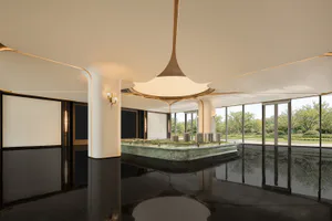 Modern luxury sales gallery interior featuring a large-scale architectural model of a residential development displayed on a green marble platform, surrounded by dramatic curved ceilings with gold accents, dark polished marble floors with perfect reflections, and floor-to-ceiling windows overlooking a landscaped garden.