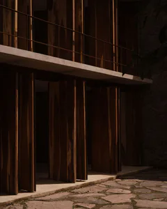 現代建築外觀，採用深色柚木垂直板材、混凝土懸挑、金屬欄杆，以及不規則石板步道，沐浴在溫暖陽光下。