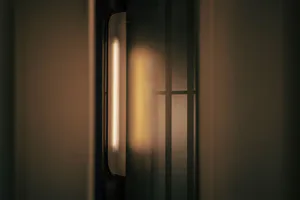 Close-up of a modern vertical brushed metal wall sconce emitting a warm vertical light beam in a dimly lit interior space.