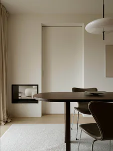 Modern minimalist dining area featuring a dark walnut round table, brown leather chairs, white textured rug, and a large white pendant lamp in a neutral beige interior.