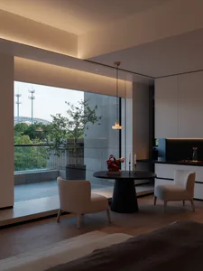 Modern minimalist living and dining area with two beige upholstered chairs, a round black pedestal table, large floor-to-ceiling windows overlooking green hills and city infrastructure, light oak flooring, and warm ambient ceiling lighting.
