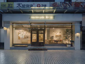 夜晚的現代極簡茶飲店面，大片玻璃窗、木門、白色磁磚外牆，以及亮起的喜茶工藝招牌。