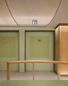 Modern reception area featuring a curved light-wood desk against sage green walls with gold accent sconces and fabric-wrapped ceiling