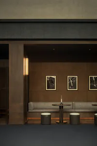 Modern lounge interior with dark wood paneling, a gray upholstered banquette, round marble-top table, cylindrical stools, vertical wall sconce, and three framed black-and-white pickleball photographs on the wall.
