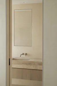 Modern minimalist bathroom with a floating travertine stone vanity, integrated sink, wall-mounted brushed nickel faucet, large frameless mirror, and textured beige plaster walls.