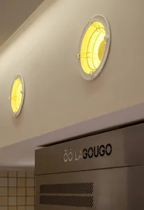 Two circular yellow-glowing porthole wall lights mounted on a beige wall above a stainless steel range hood with the brand name LAGOUGO.