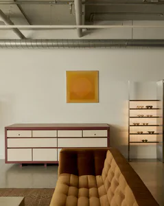 Modern living room featuring a terracotta and cream console table, mustard velvet tufted sofa, glowing sunglasses display shelf, and large abstract ochre circular artwork.