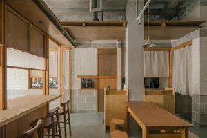 Industrial-style cafe interior with exposed concrete ceiling, oak wood counters and tables, wooden stools, and white brick walls in Taiwan.