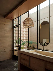 Modern minimalist bathroom featuring a concrete wall and ceiling, wooden rattan pendant light, terrazzo vanity with wooden rattan cabinet, black matte faucet, and large steel windows opening to a courtyard with tropical plants.