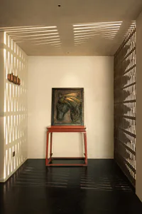 A minimalist entryway featuring a bronze horse head relief sculpture displayed on a red wooden console table, with strong sunlight creating striped shadows on white walls and dark reflective floor.