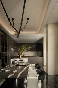 Modern luxury dining room with a long black and white marble dining table, white and black dining chairs, a sculptural black and glass chandelier, and a kitchen island with floral arrangement in the background.
