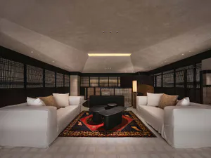 Modern Japanese-style lounge featuring two white sofas facing each other across a dark coffee table on a patterned oriental rug, with textured plaster walls and ceiling, dark wood shoji screens, and warm ambient lighting.