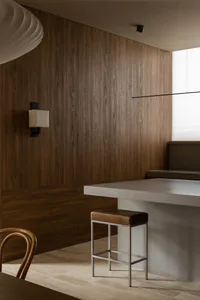 Modern minimalist kitchen featuring a dark walnut wood paneled wall, a concrete kitchen island, a brown leather bar stool with metal frame, and a sculptural white pendant light.