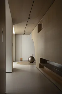 Modern minimalist hallway featuring light oak wood paneling, built-in lighting, a large bronze sphere sculpture, and a circular wood inlay on the floor.