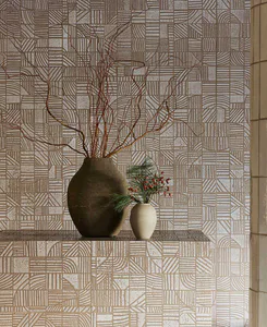 Still life arrangement on a textured shelf featuring a large dark earthenware vase with twisted brown branches and a small off-white ceramic vase with pine and red berries, set against a wall of beige and white geometric patterned tiles.