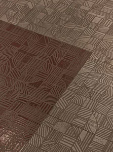 Close-up view of two different colored ceramic floor tiles with intricate geometric and linear patterns, one in deep burgundy and the other in metallic taupe.